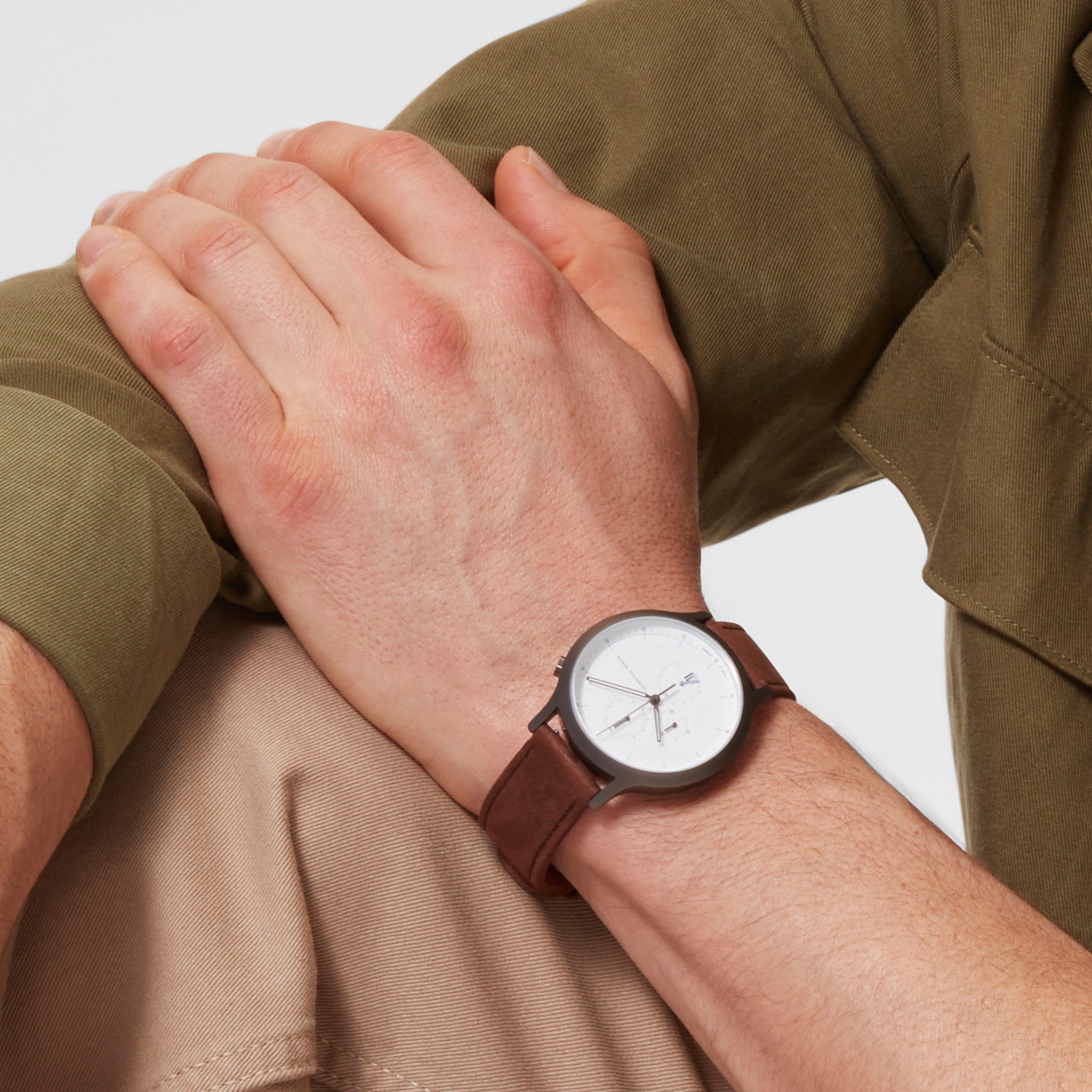 Minimalist men's wristwatch with white dial, brown leather strap, worn on wrist