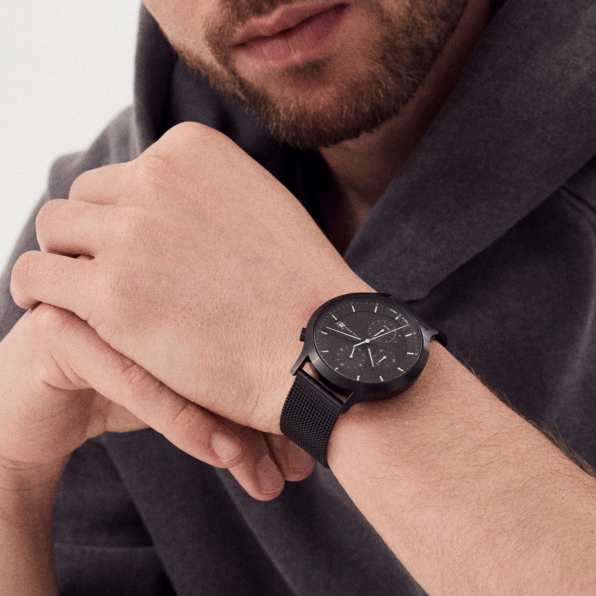 Man wearing a modern black minimalist wristwatch with mesh band and dark dial
