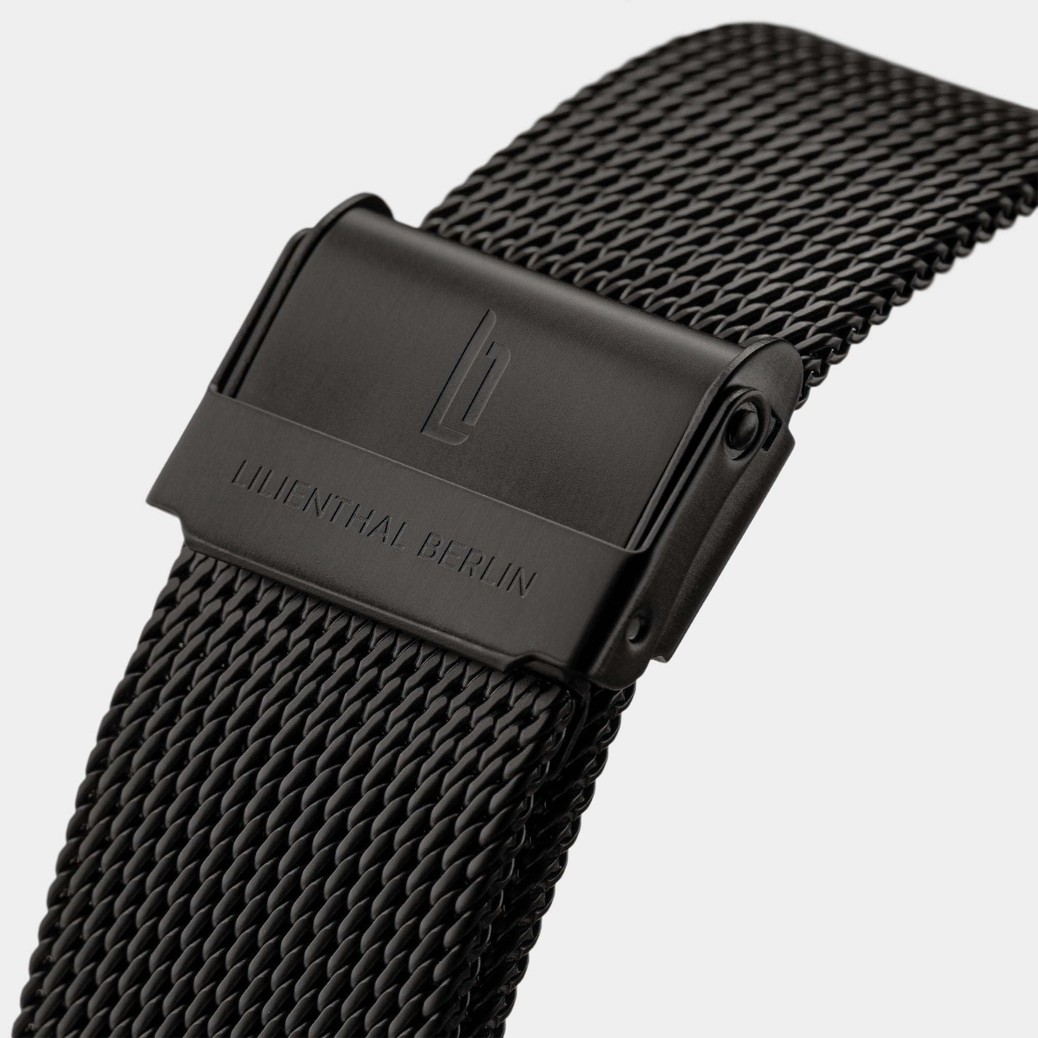Black stainless steel mesh watch strap with engraved clasp, close-up view