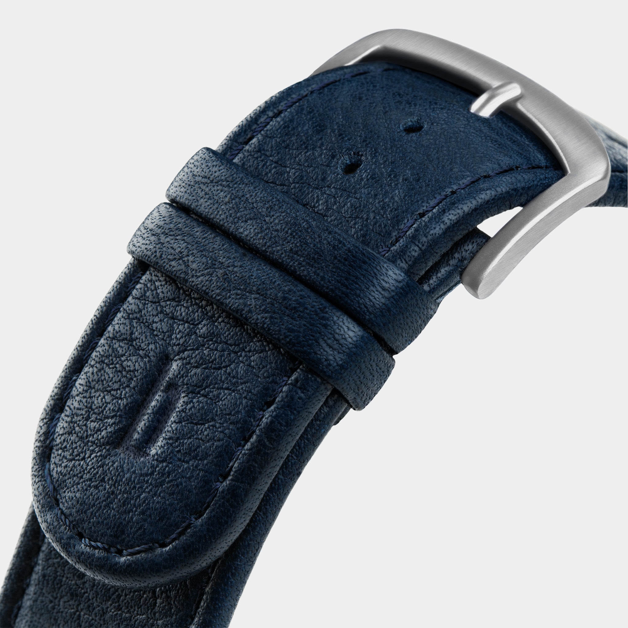 Close-up of a navy blue textured leather watch strap with a silver buckle