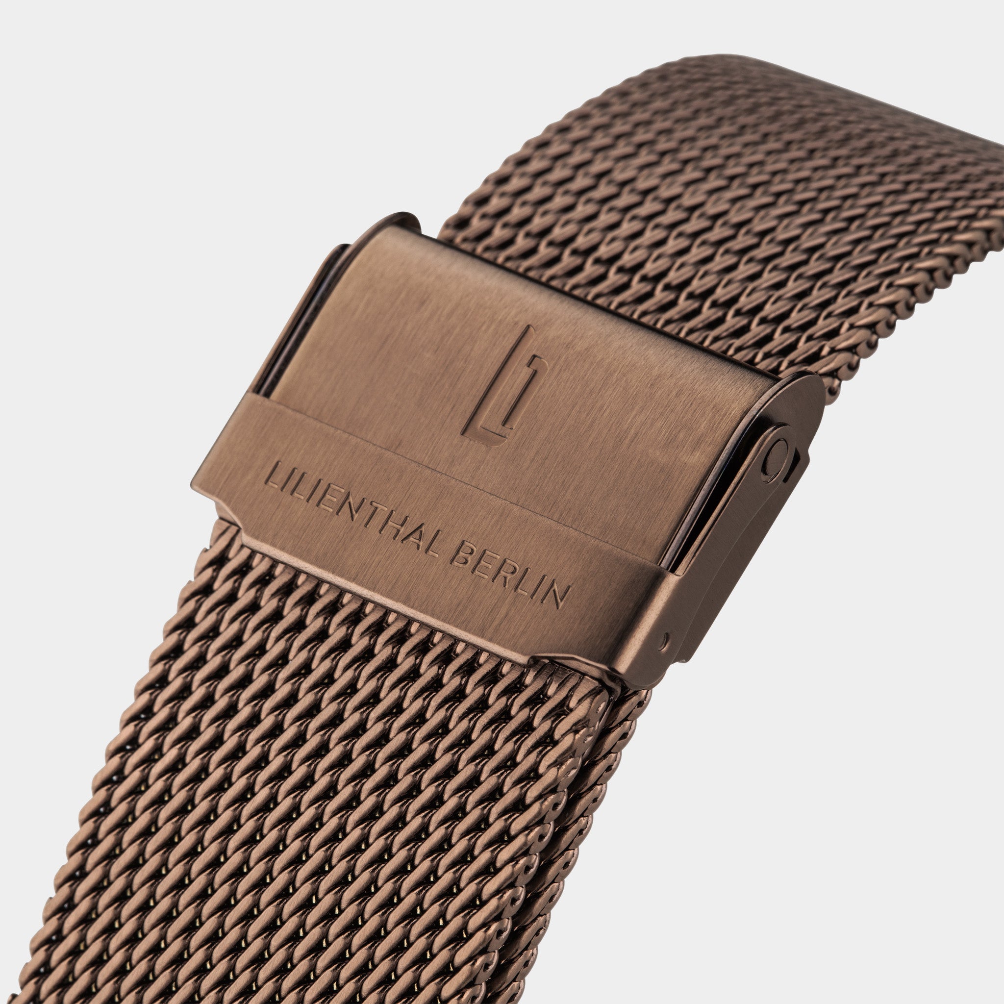 Close-up of bronze mesh watch strap with engraved clasp and modern design.