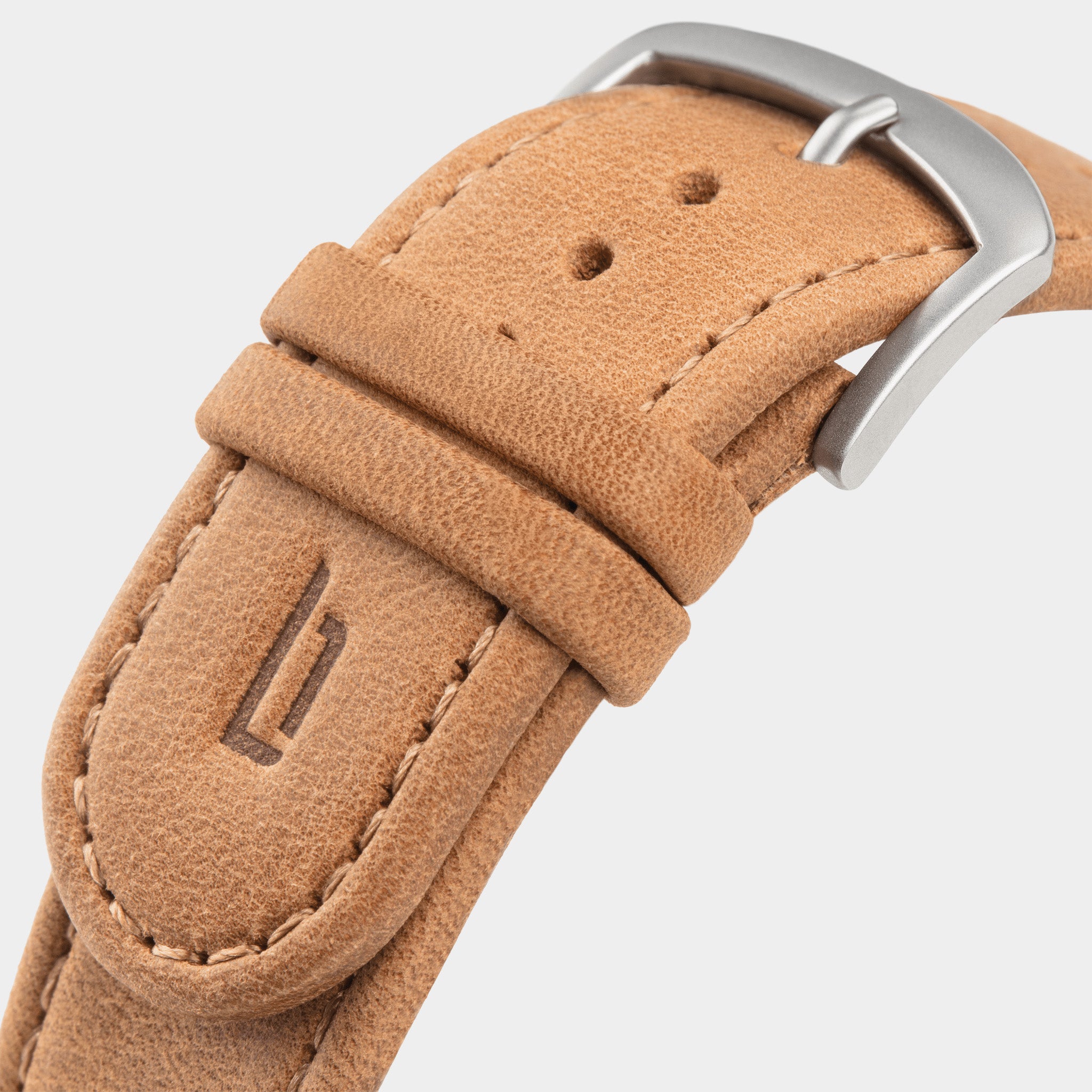Close-up of tan leather watch strap with metal buckle and embossed decorative emblem