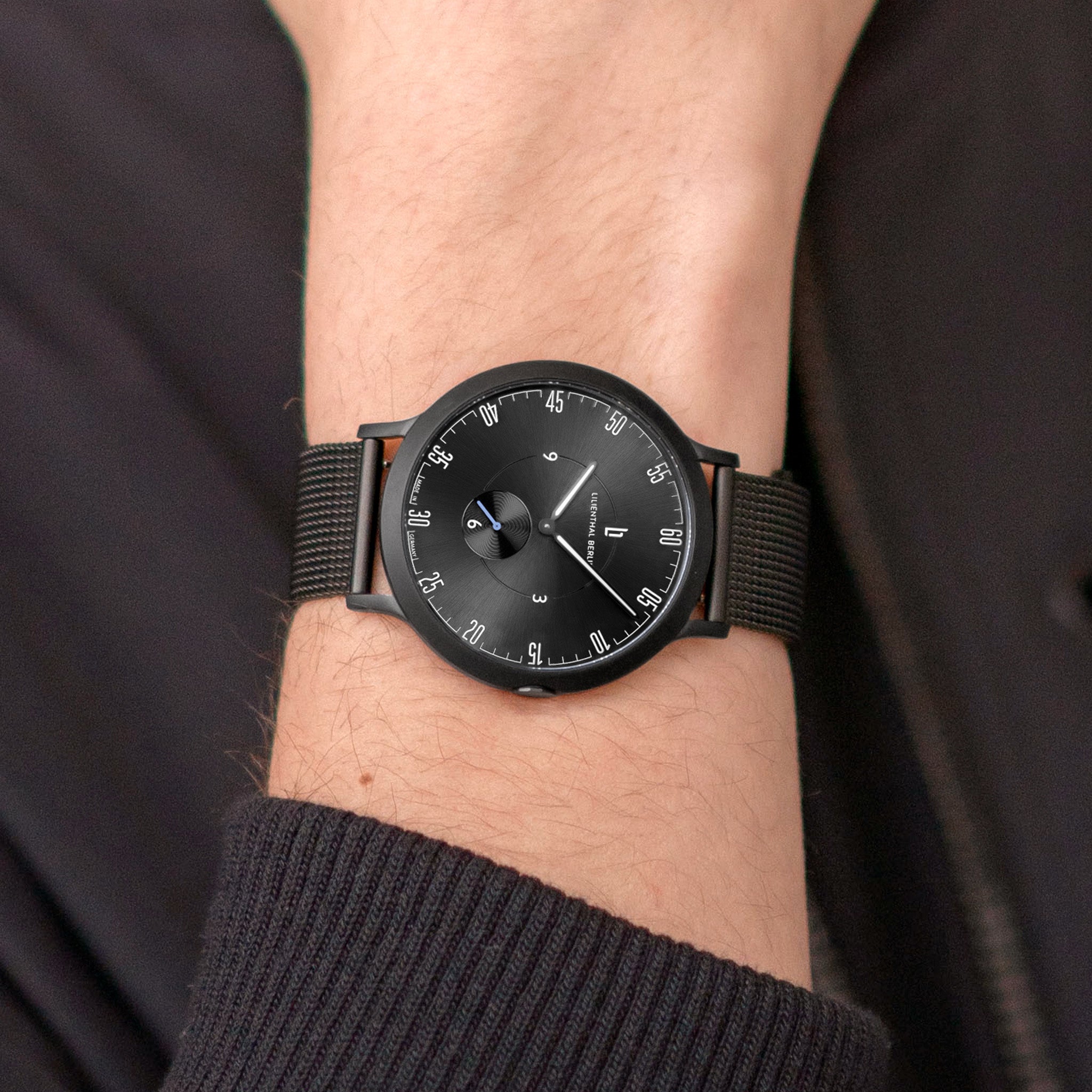 Minimalist black analog watch with mesh band on wrist, modern and stylish design