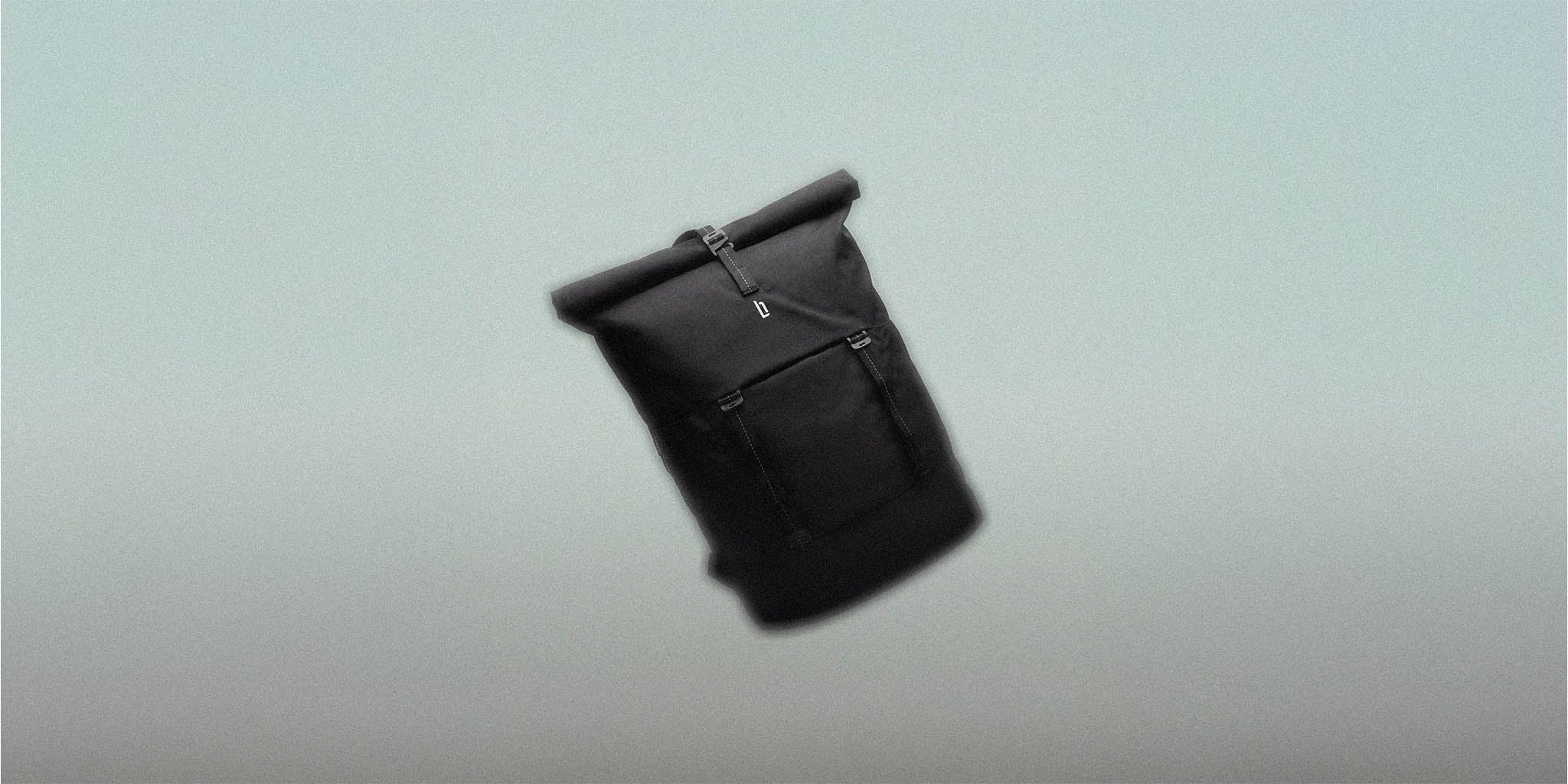 Black rolltop backpack with front pocket on a minimalist grey background