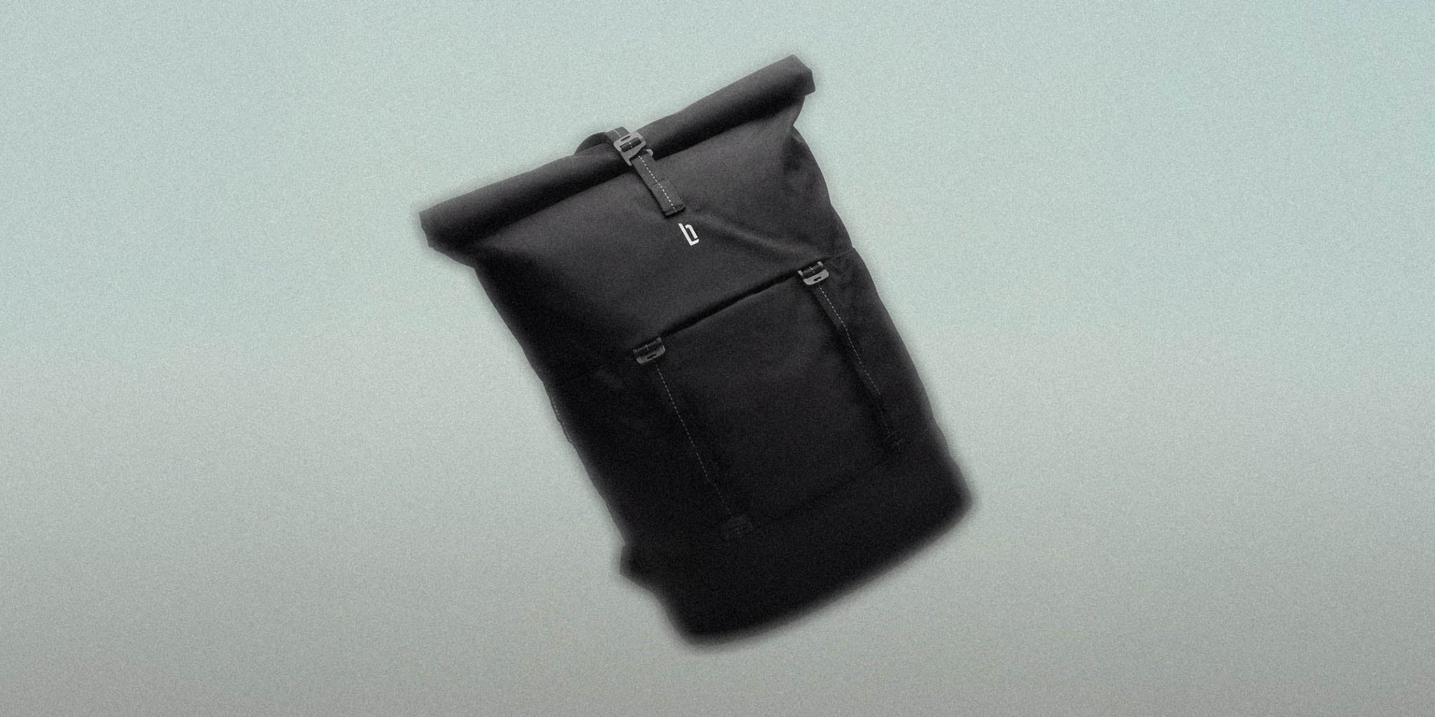 Black rolltop backpack with buckle closure and front pocket on light background