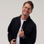 Smiling man in glasses wearing a black jacket, white shirt, and blue wristwatch