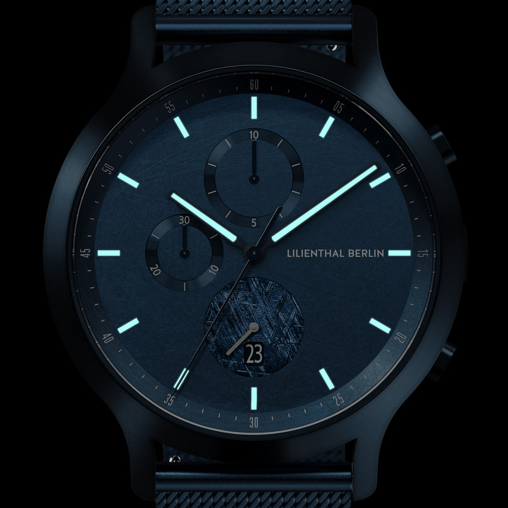 Modern blue chronograph watch with luminous markers and subdials on a dark background