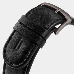Close-up of a black leather watch strap with a matte metal buckle on a light background