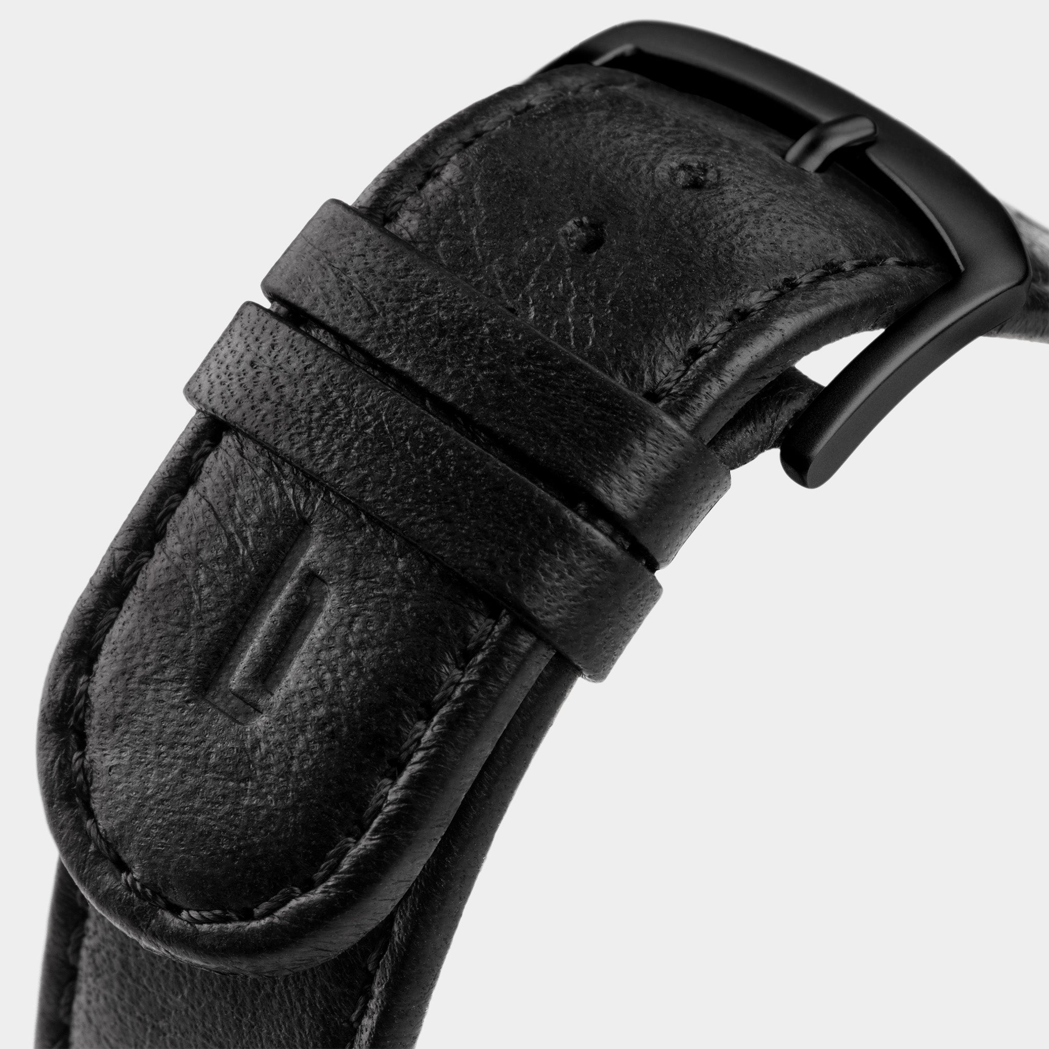 Close-up of black leather watch strap with matte black buckle on light background