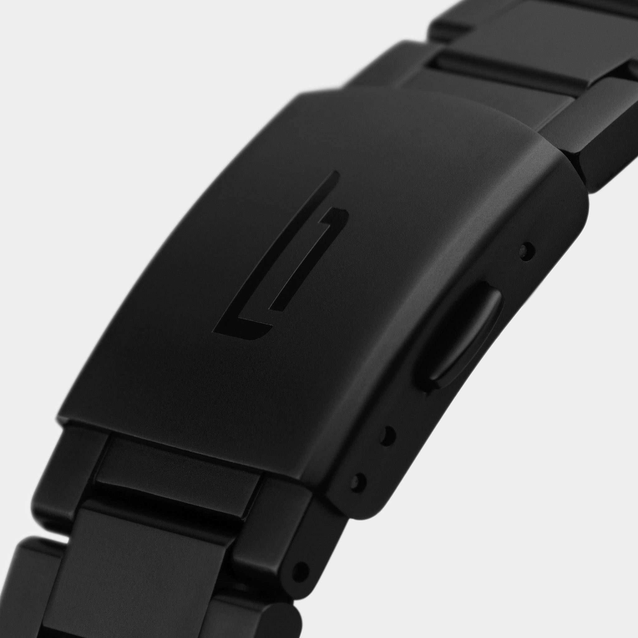 Close-up of a matte black metal watch clasp with engraved logo on a bracelet strap