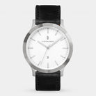 Minimalist silver wristwatch with a white dial, black leather strap, and date display.
