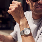 Minimalist silver wristwatch with mesh band worn on man's wrist in sunlight