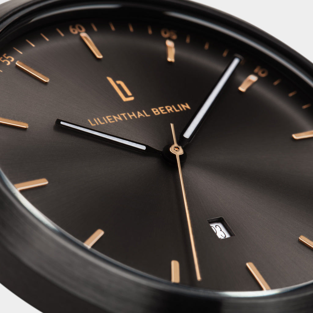 Close-up of a minimalist black watch face with gold markers and date display
