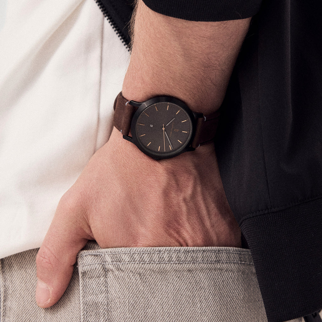 Minimalist black dial wristwatch with brown leather strap on a man's wrist