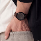 Minimalist black dial wristwatch with brown leather strap on a man's wrist