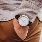 Minimalist wristwatch with white dial and black strap on wrist, casual outfit background