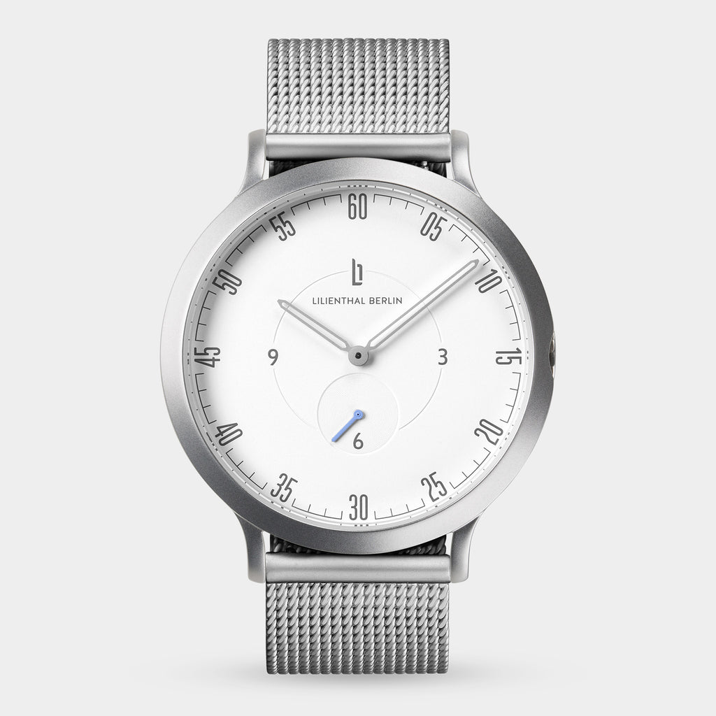 Minimalist silver mesh watch with white dial and black numerals on a light background