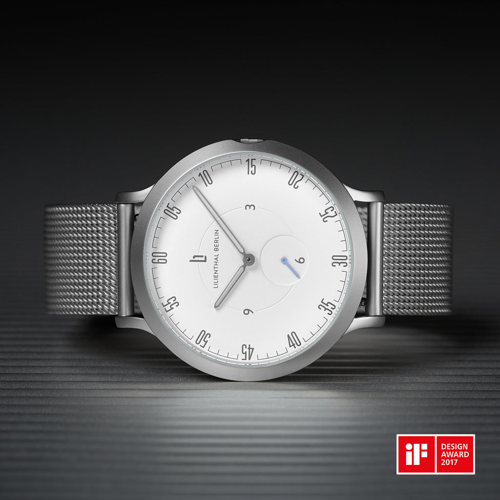 Minimalist silver mesh watch with white dial and iF Design Award 2017 badge on dark background.