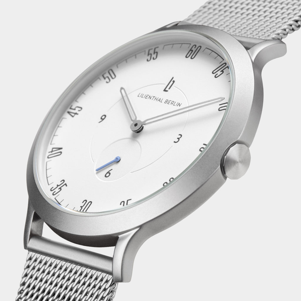 Minimalist silver mesh watch with white dial and black markers, close-up side view