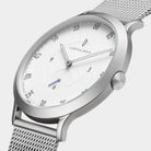 Minimalist silver mesh watch with white dial and black markers, close-up side view