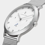 Minimalist silver mesh watch with white dial and black markers, close-up side view