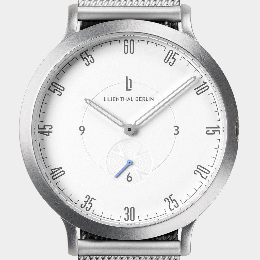 Minimalist silver wristwatch with white dial, mesh strap, and modern hour markers.