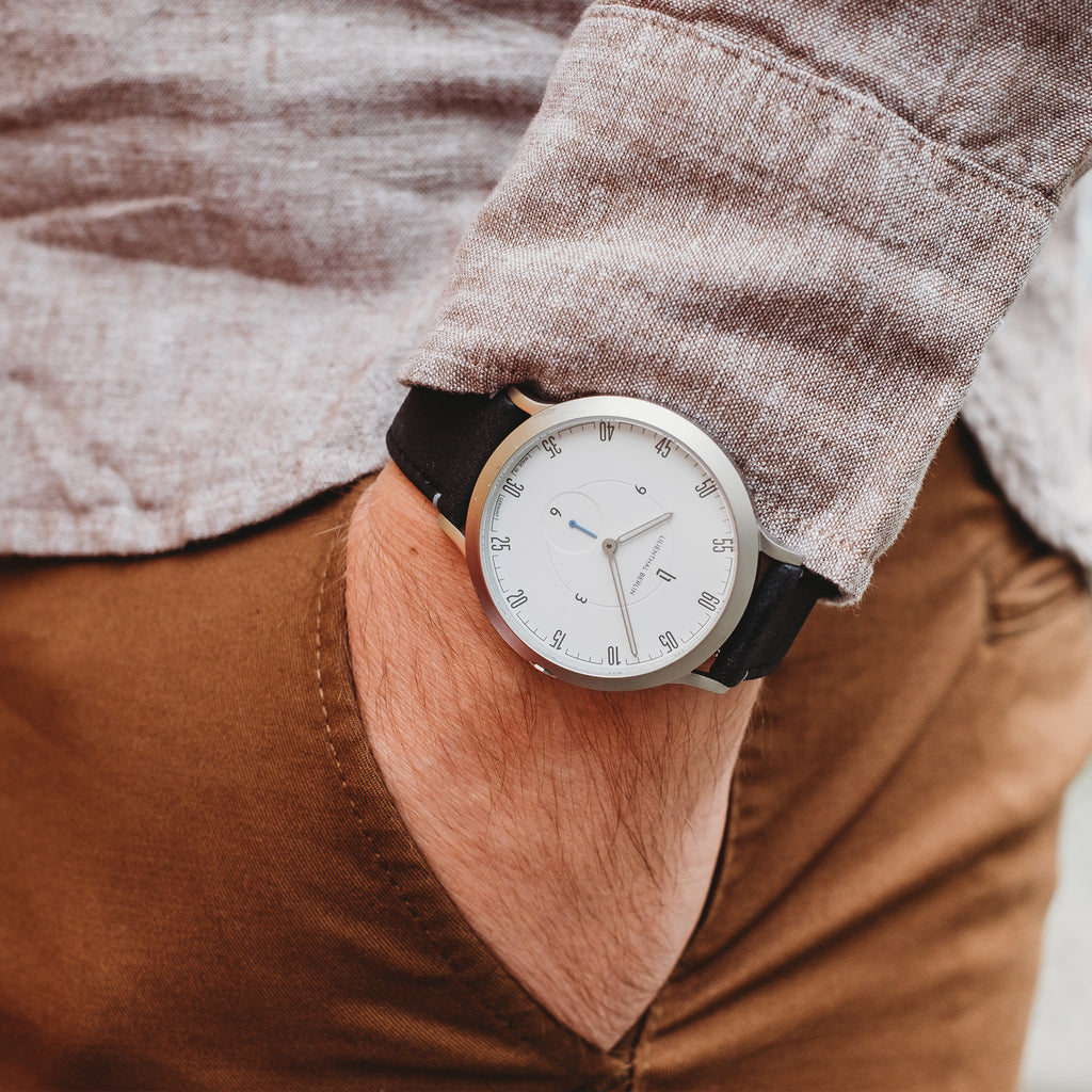 Minimalist silver wristwatch with white dial and black strap on wrist, casual outfit