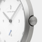 Minimalist silver watch with white dial, sleek hands, and brushed metal crown close-up
