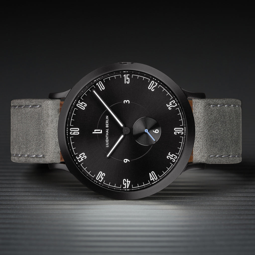 Minimalist black watch with grey leather strap, modern dial, and distinctive white markers