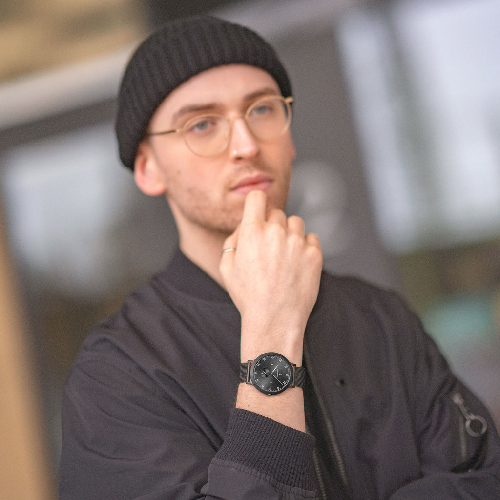 Man wearing black minimalist watch, black beanie, and glasses in urban setting