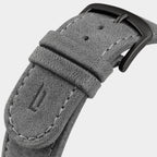 Close-up of grey suede watch strap with black buckle and visible stitching