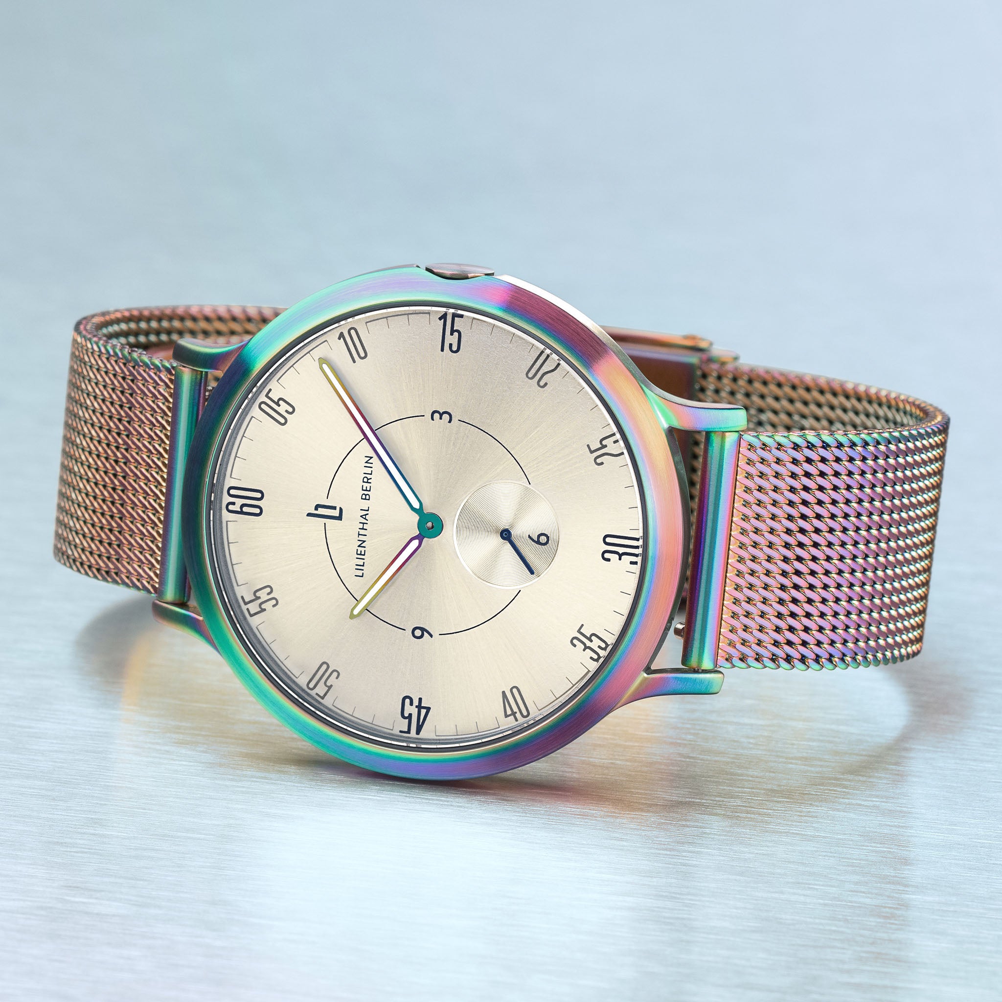 Elegant mesh band watch with metallic rainbow bezel and minimalist dial on a silver surface