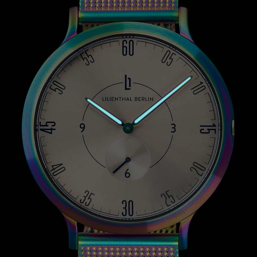 Minimalist analog watch with iridescent case and mesh strap, black dial, luminous hands