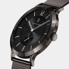 Minimalist black wristwatch with mesh strap and silver hour markers on white background