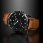 Minimalist black watch with round case and brown leather strap on dark background